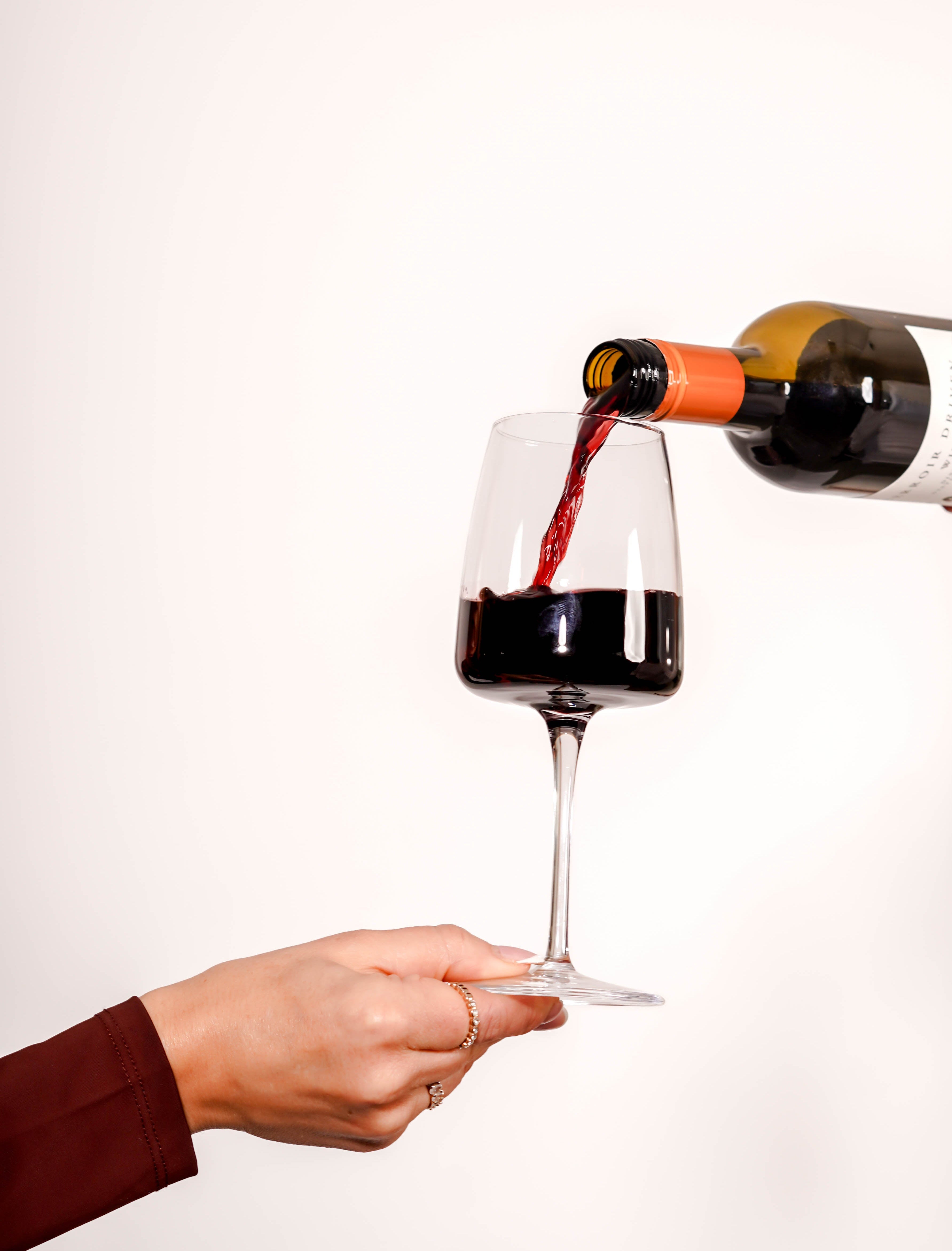Person pouring red wine from a bottle into a glass against a white background