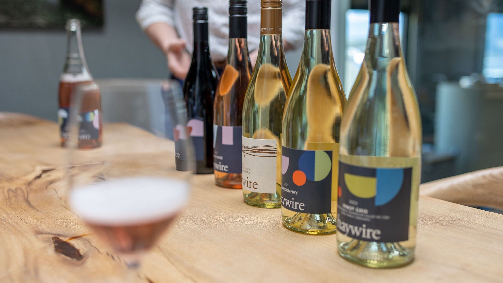 Haywire Wine bottles on a wooden table with a person in the background